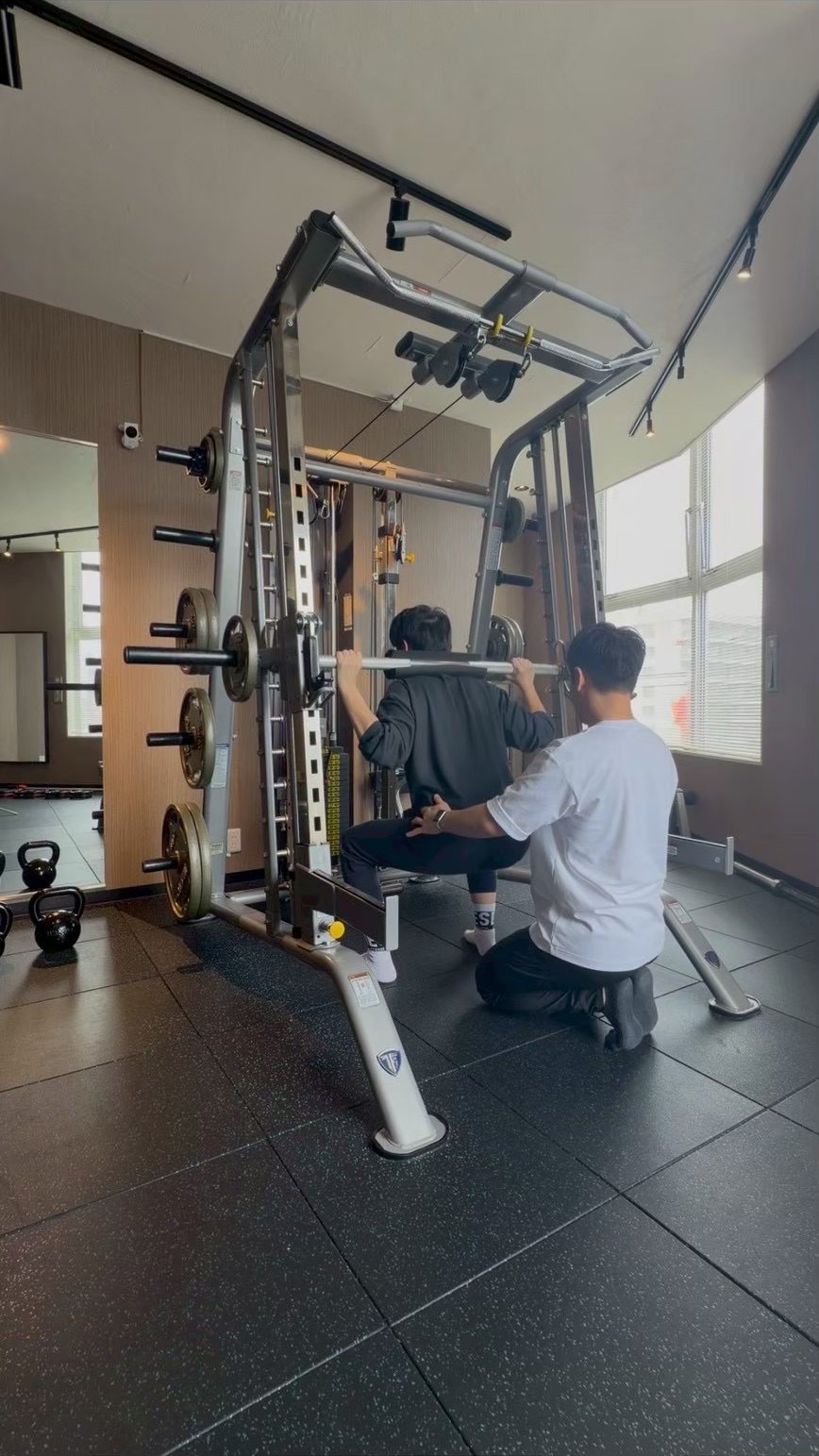 スミスマシンでのスクワットをトレーナーが横でフォーム確認している様子
